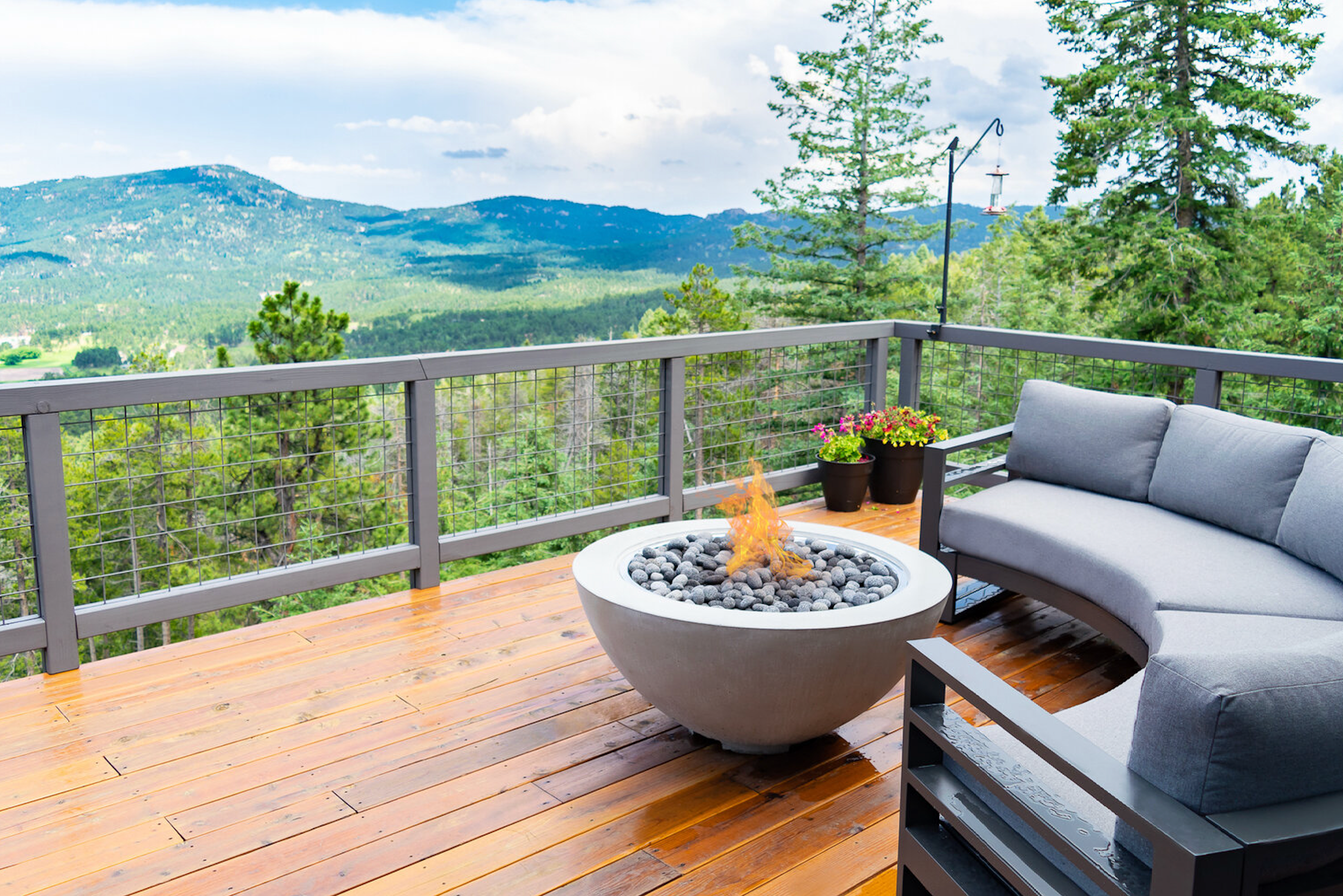 A Cove fire bowl on a deck overlooking a mountain scene. A round outdoor sofa sits behind it.
