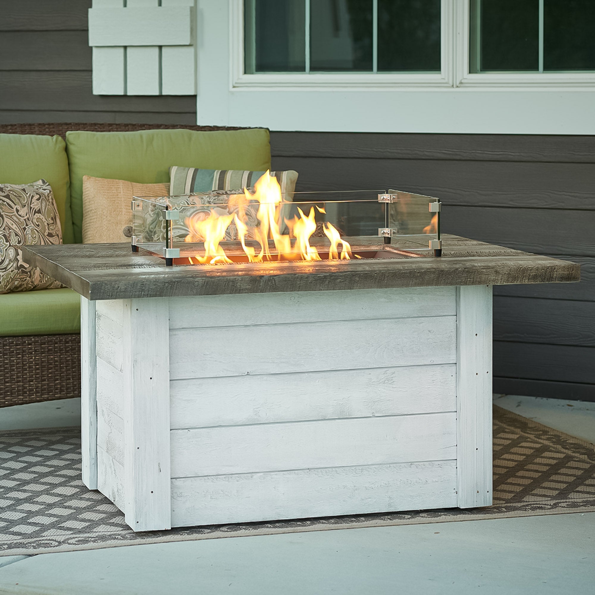 A glass wind guard placed on a Alcott Rectangular Gas Fire Pit Table to protect the large flame from the wind
