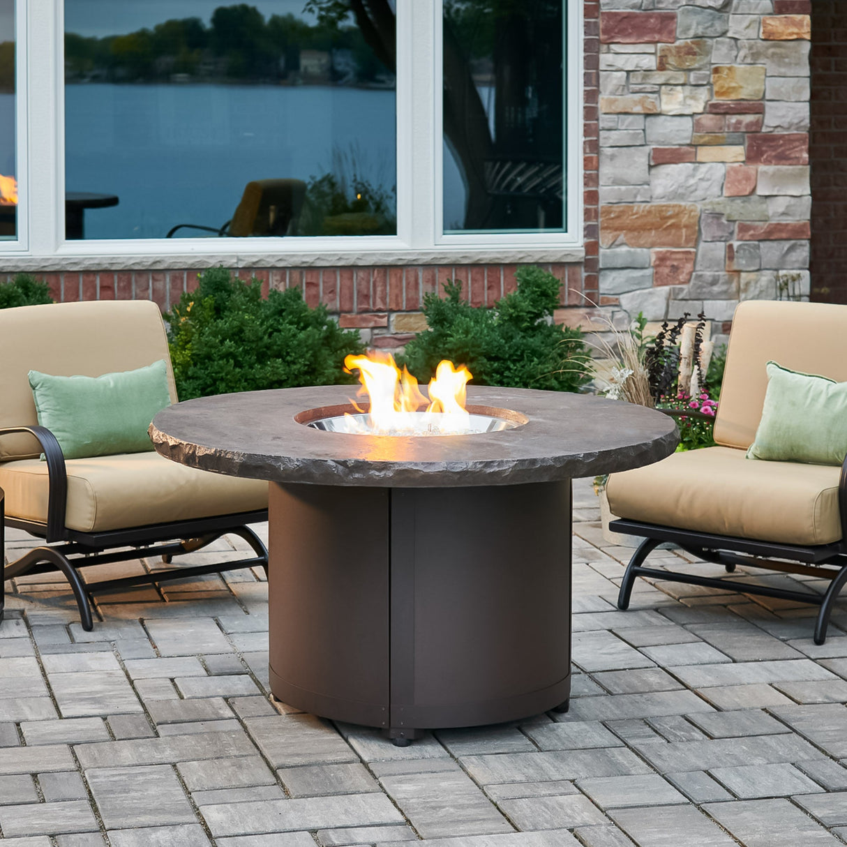 The Marbleized Noche Beacon Round Gas Fire Pit Table outside next to outdoor furniture