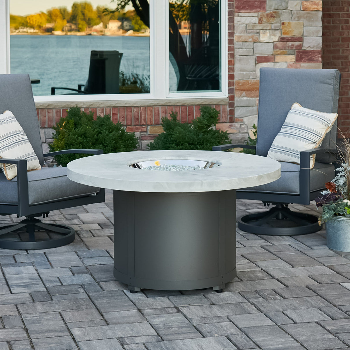 The White Onyx Beacon Round Gas Fire Pit Table with its cover off next to patio furniture outside