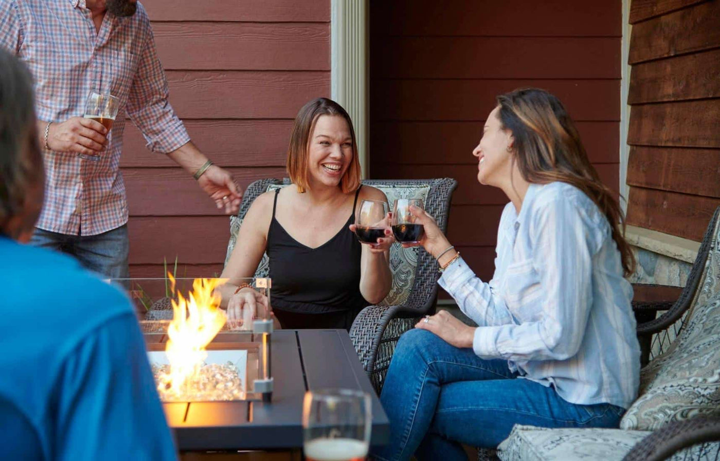Individuals gathered around a fire pit table and enjoy a drink and conversation