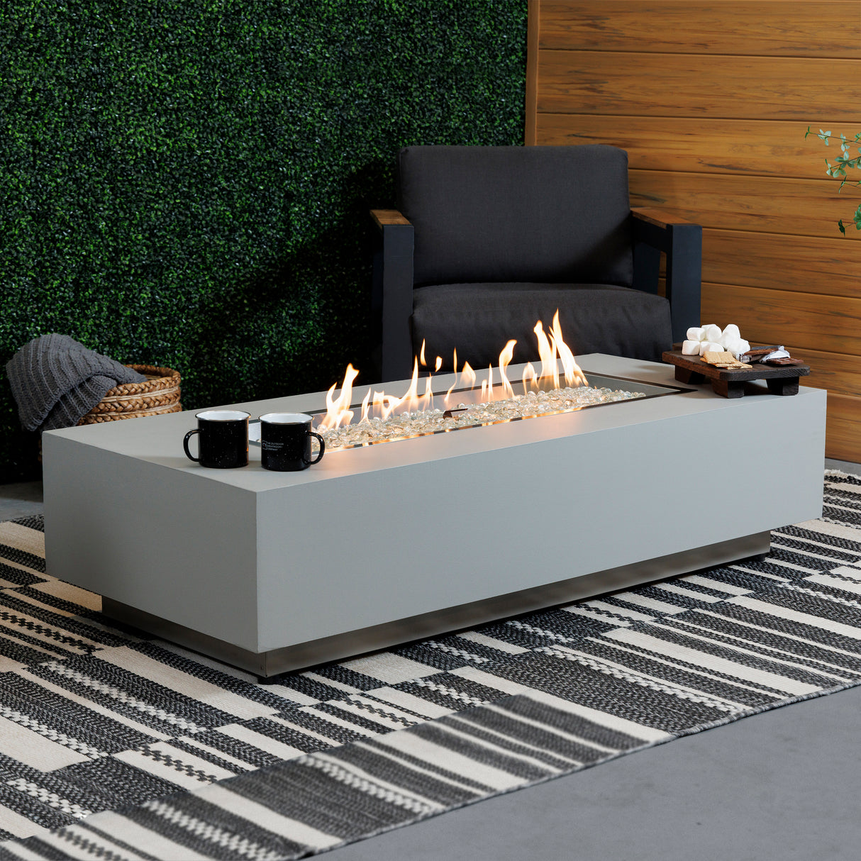 A side view of the Harbor View Rectangular Gas Fire Pit Table in a modern patio setup with food and drink on the top of the table