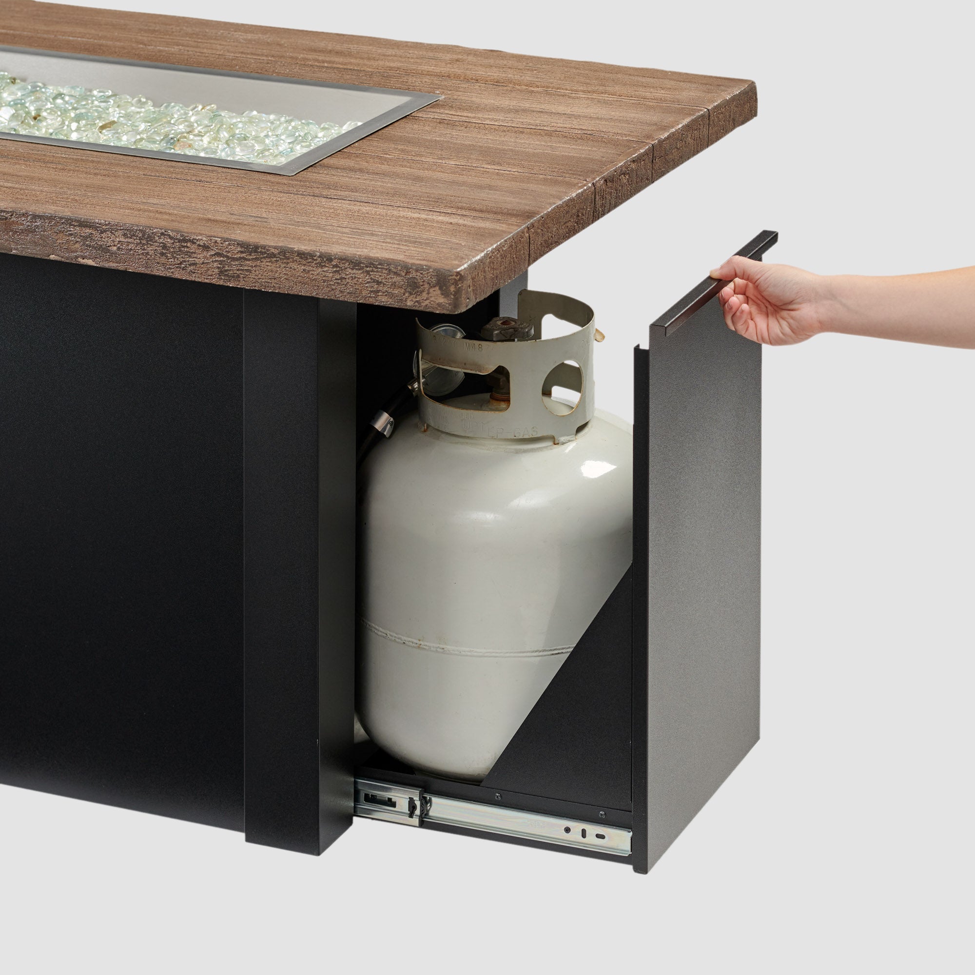 The side access door being opened on a Havenwood Linear Gas Fire Pit Table with a Driftwood top and Luverne Black base on a grey background