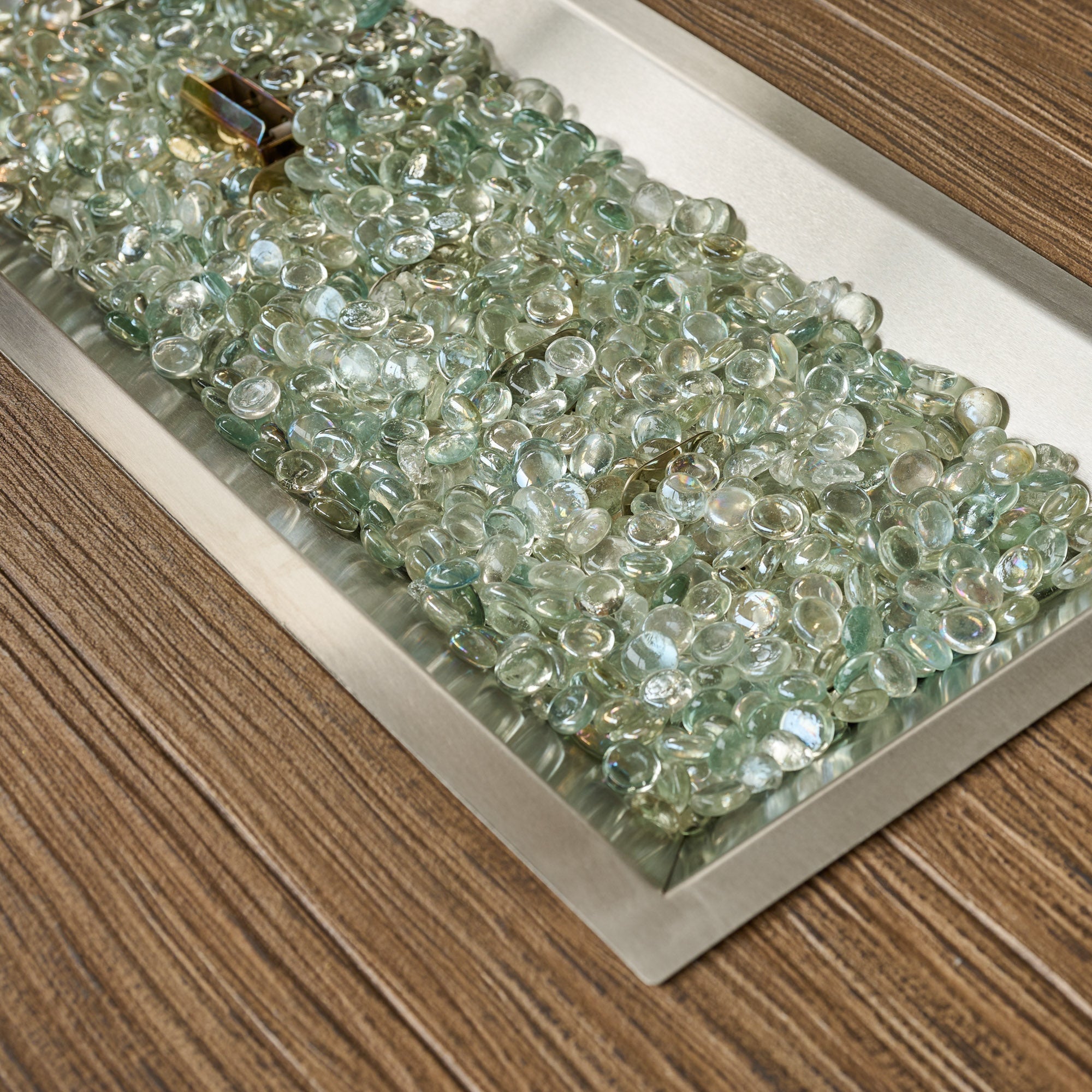 A close up of fire gems in the burner of a Havenwood Linear Gas Fire Pit Table with a Driftwood top and Luverne Black base