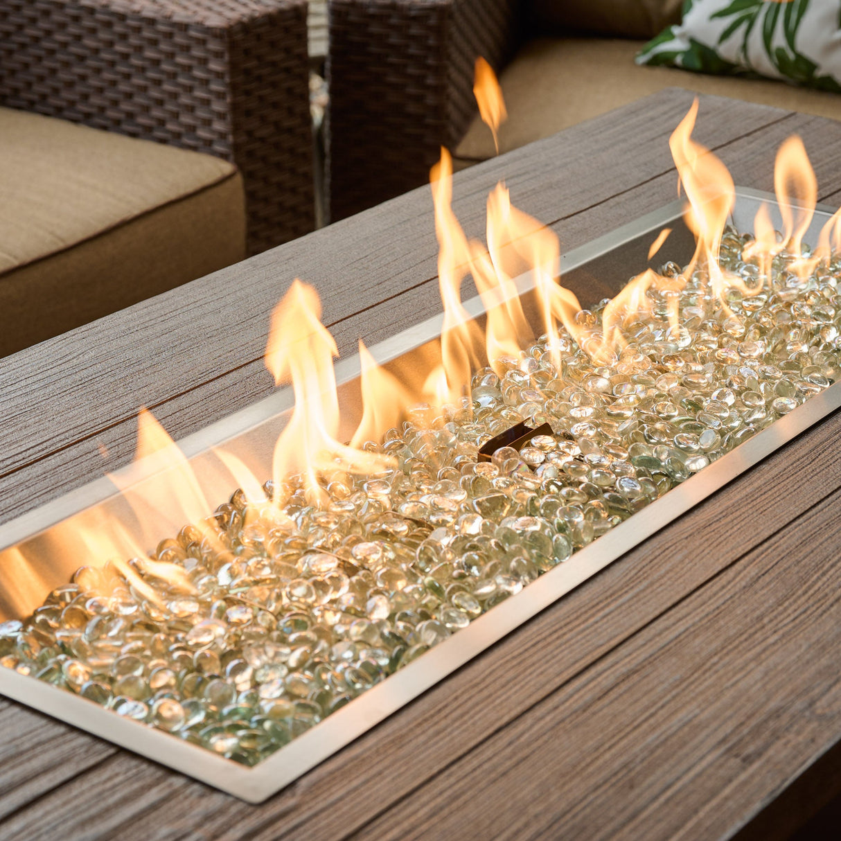 A close up of the flame coming from the burner of a Havenwood Linear Gas Fire Pit Table with a Driftwood top and Luverne Black base