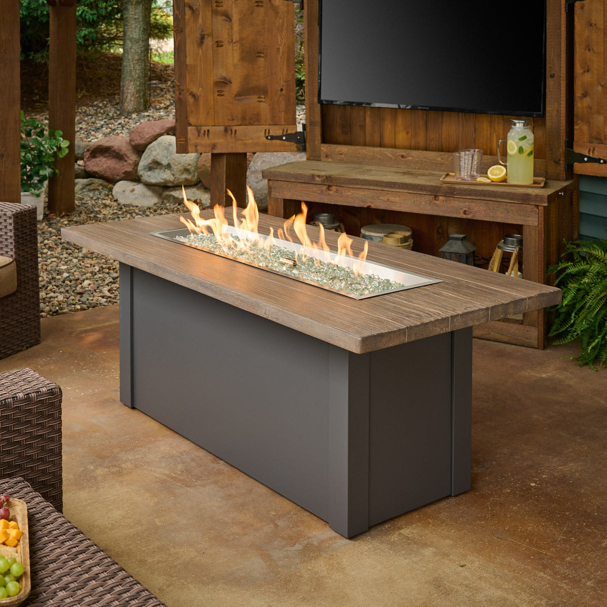 The Havenwood Linear Gas Fire Pit Table with a Driftwood top and Graphite Grey base in a scenic patio setting
