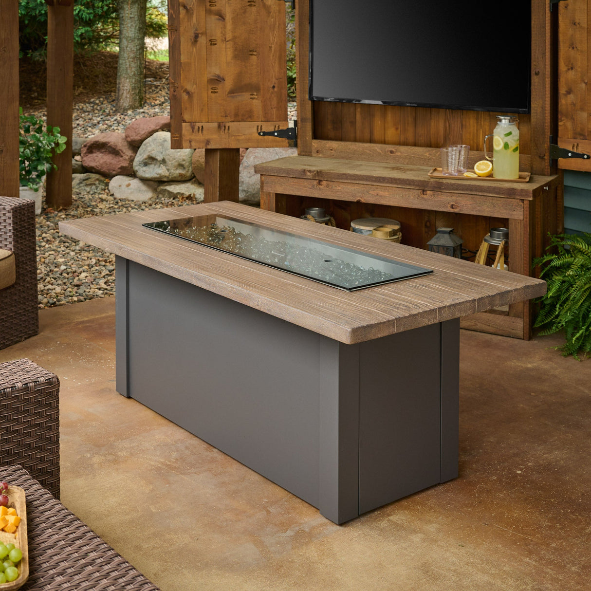The Havenwood Linear Gas Fire Pit Table with a Driftwood top and Graphite Grey base being used as a table with its cover placed on the burner