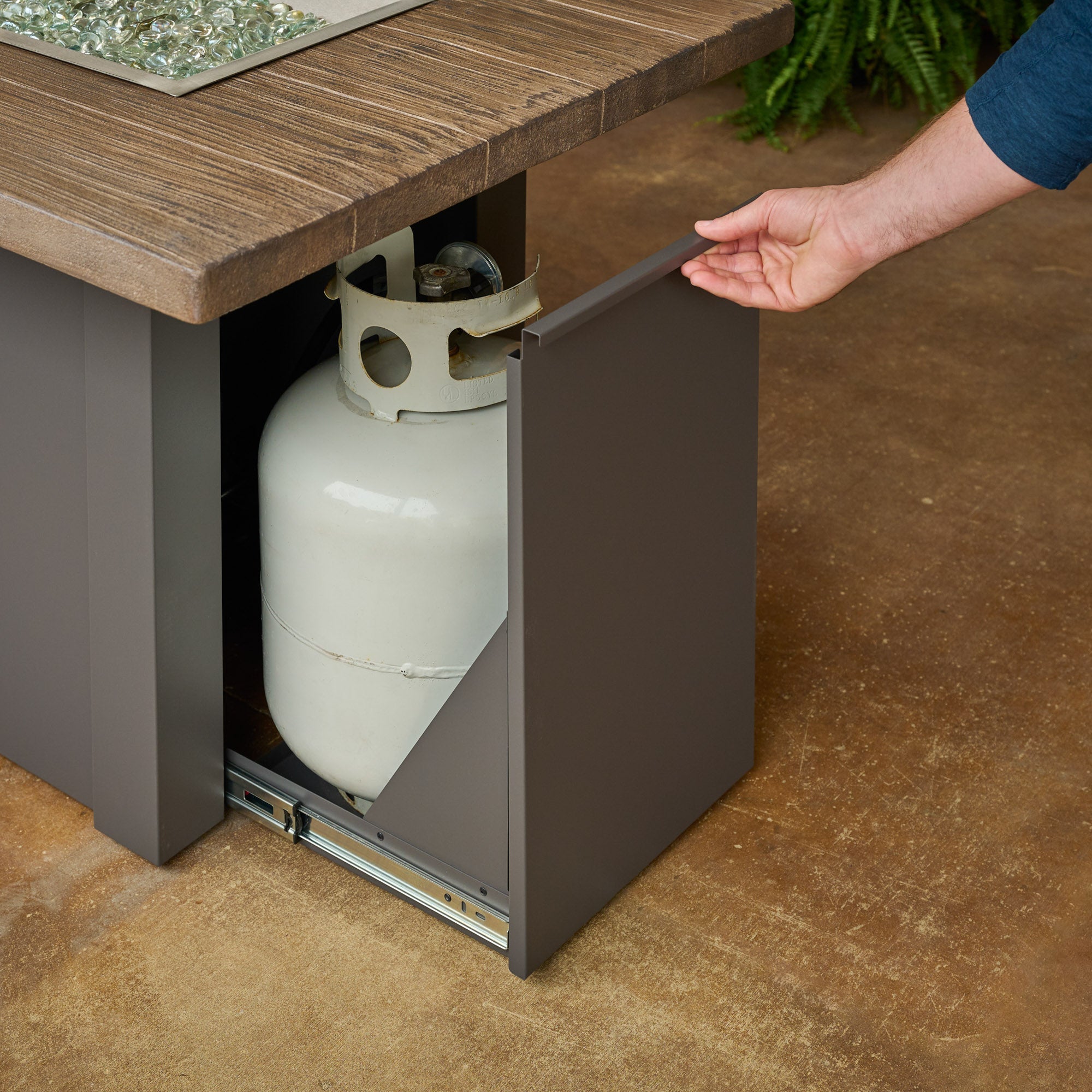 An individual opening the side access door on a Havenwood Linear Gas Fire Pit Table with a Driftwood top and Graphite Grey base
