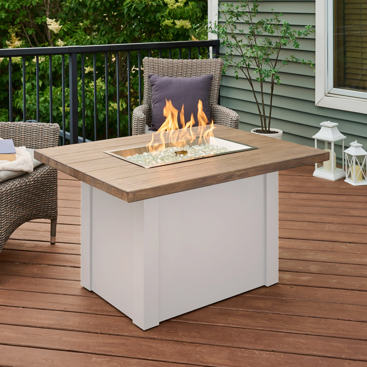 A large flame coming from the burner of a Havenwood Rectangular Gas Fire Pit Table with a Driftwood top and White base on a patio