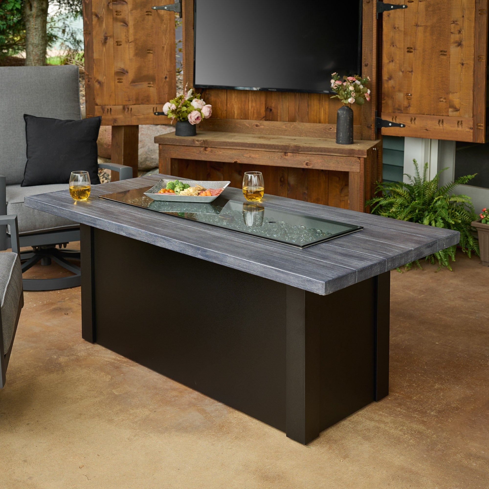 Food and drink placed on top of the Havenwood Linear Gas Fire Pit Table with a Carbon Grey top and Luverne Black base in a patio setting