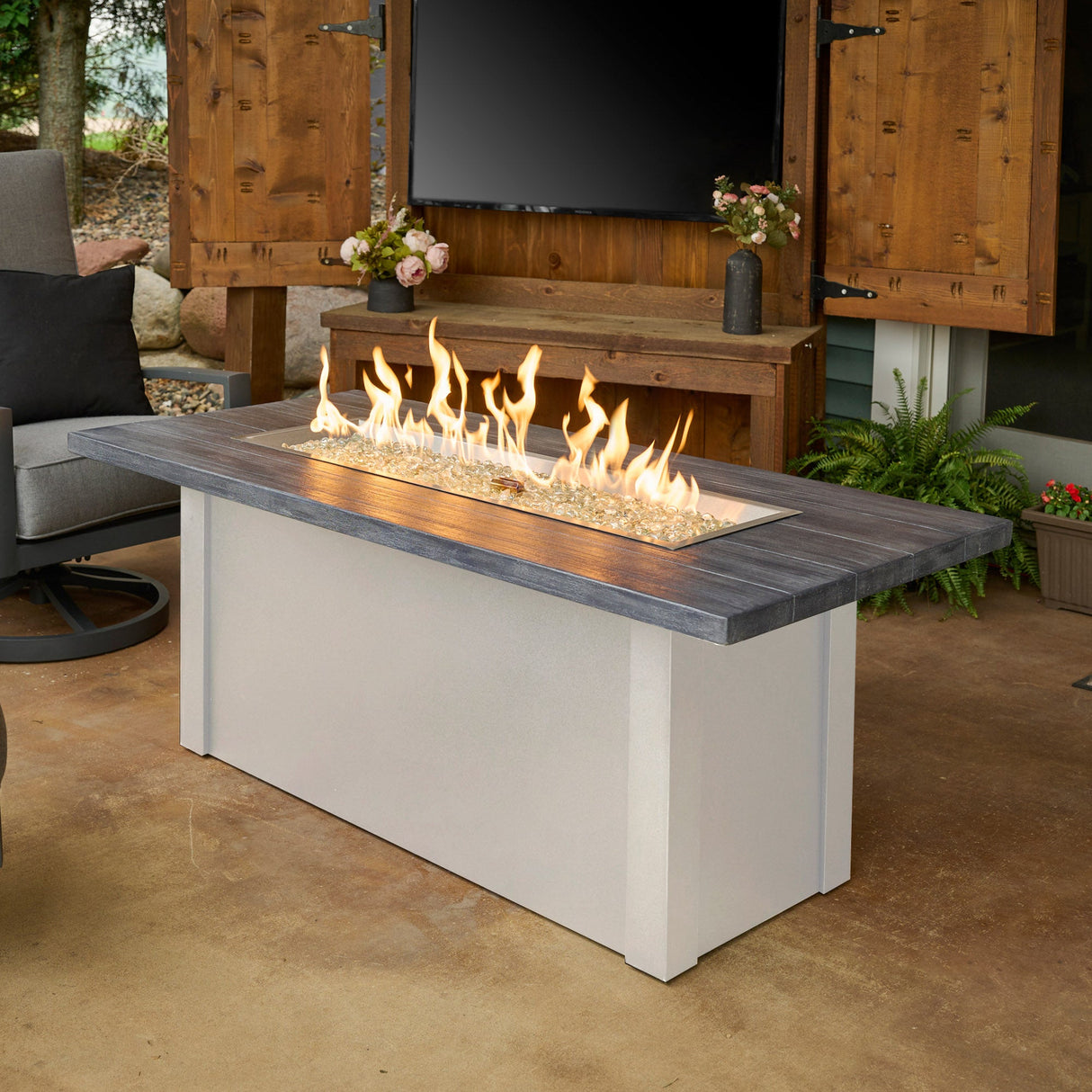 Havenwood Linear Gas Fire Pit Table with a Carbon Grey top and White base next to an outdoor patio setup