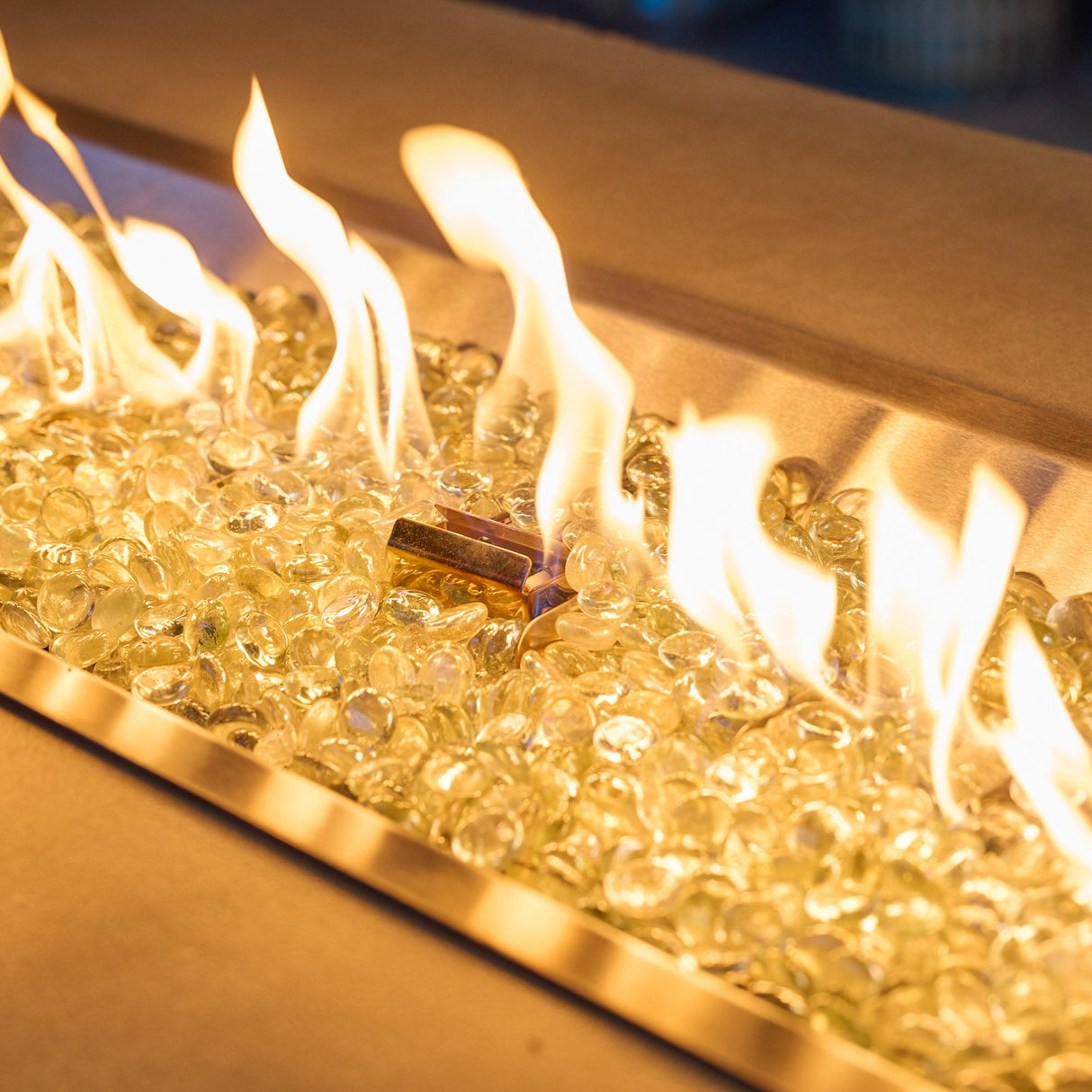 A close up of the flame coming from a Havenwood Linear Gas Fire Pit Table with a Pebble Grey top and White base