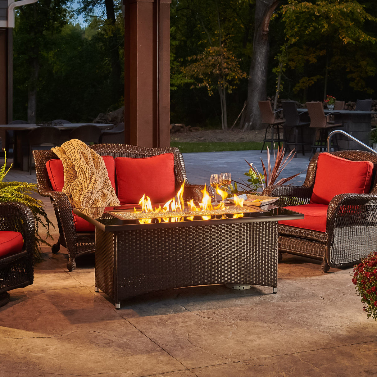 The Montego Linear Gas Fire Pit Table in a scenic patio set up with flowers and patio furniture