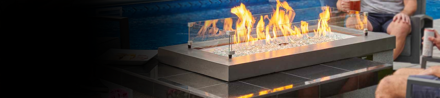Individuals sitting next to a pool and enjoying a drink by a black Uptown Linear Gas Fire Pit Table