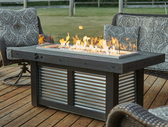 The Denali Brew Linear Gas Fire Pit Table on an outdoor patio setup next to patio furniture