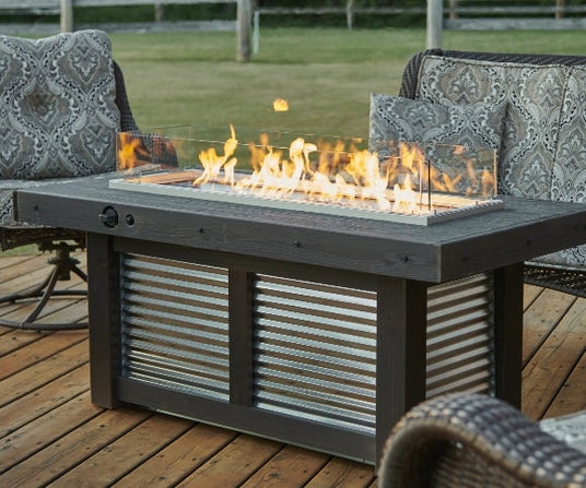 The Denali Brew Linear Gas Fire Pit Table surrounded by some patio furniture on a deck