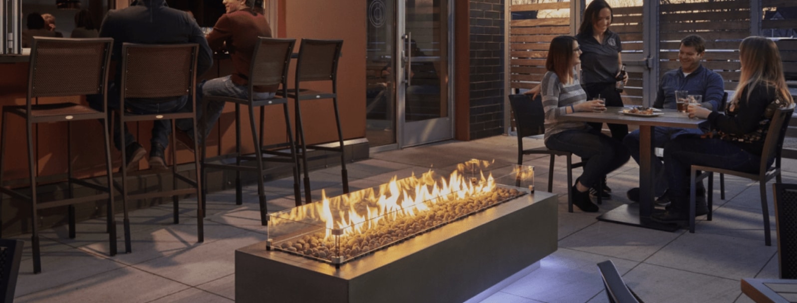A commercial space using a Cove Linear Gas Fire Pit Table near patrons enjoying a dinner