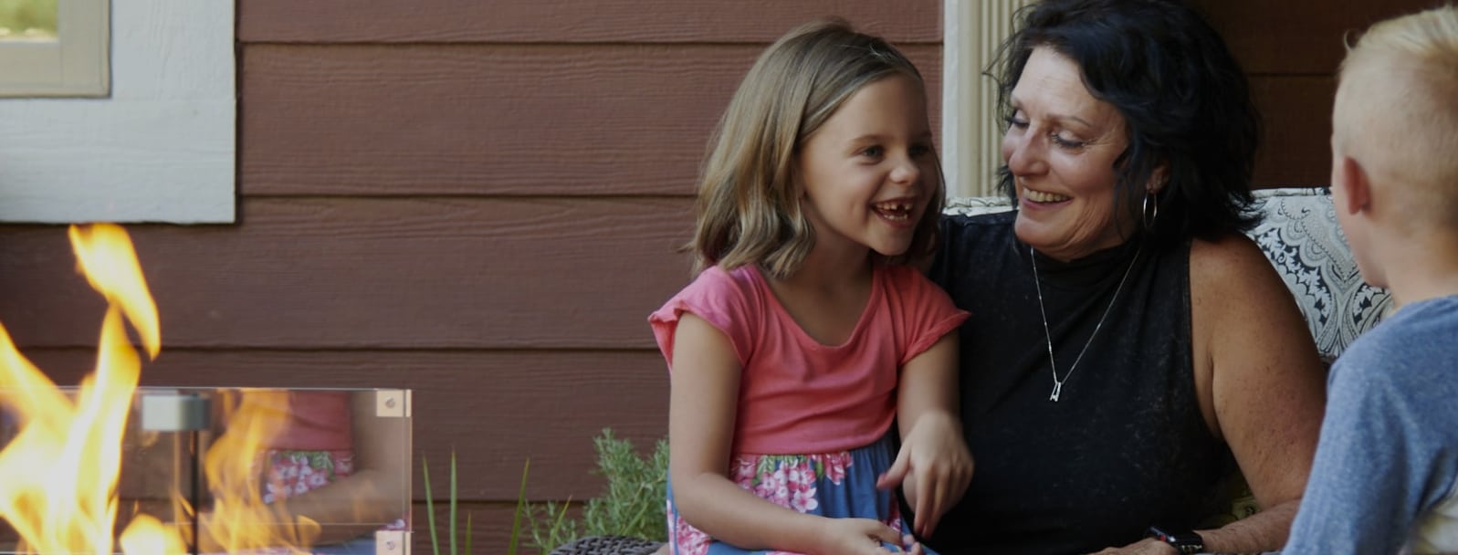 Two children and an individual next to a fire pit table outside