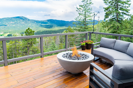 A Cove fire bowl on a deck overlooking a mountain scene. A round outdoor sofa sits behind it.