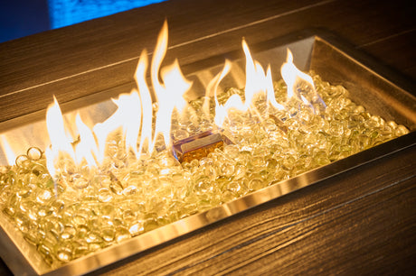 A vibrant, yellow flame burns from a Crystal Fire Plus burner in a Havenwood gas fire pit table.