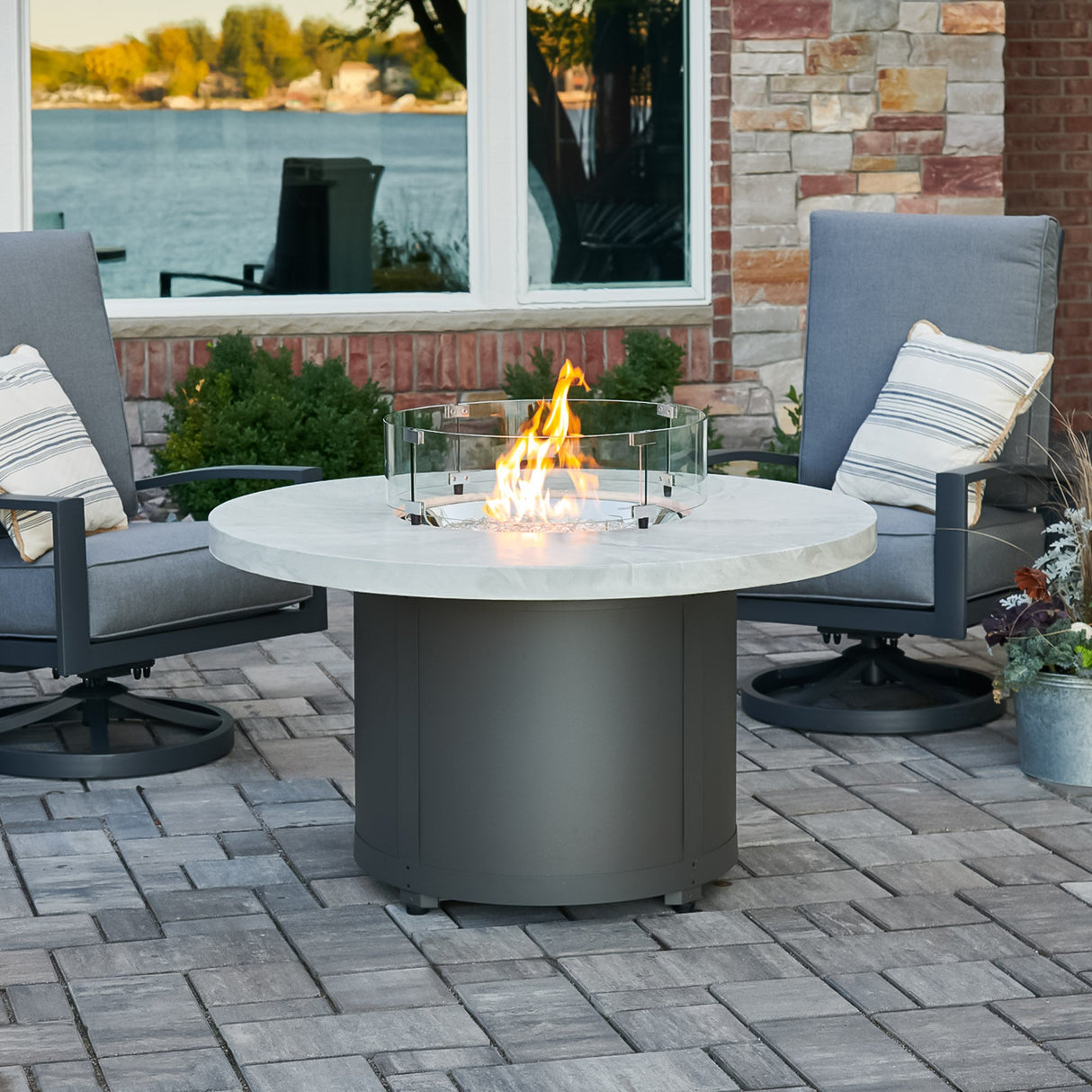 The White Onyx Beacon Round Gas Fire Pit Table with a round glass wind guard being used to protect the flame