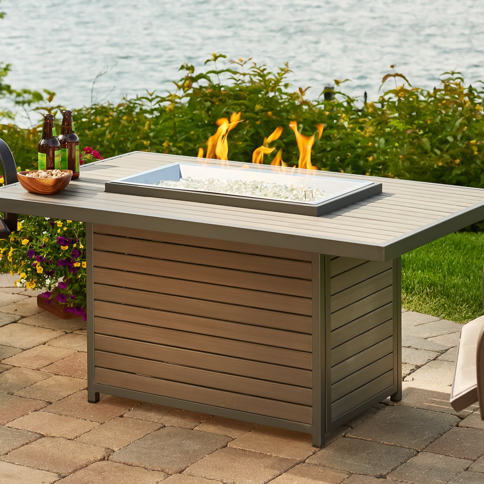 The Brooks Rectangular Gas Fire Pit Table being used as an outdoor table next to a lake