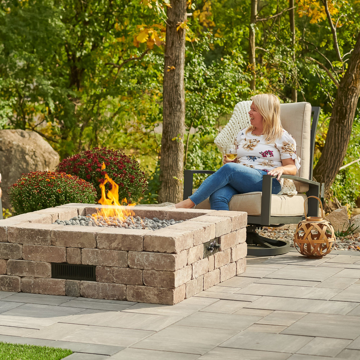 An individual relaxing next to the Bronson Block Square Gas Fire Pit Kit on a patio