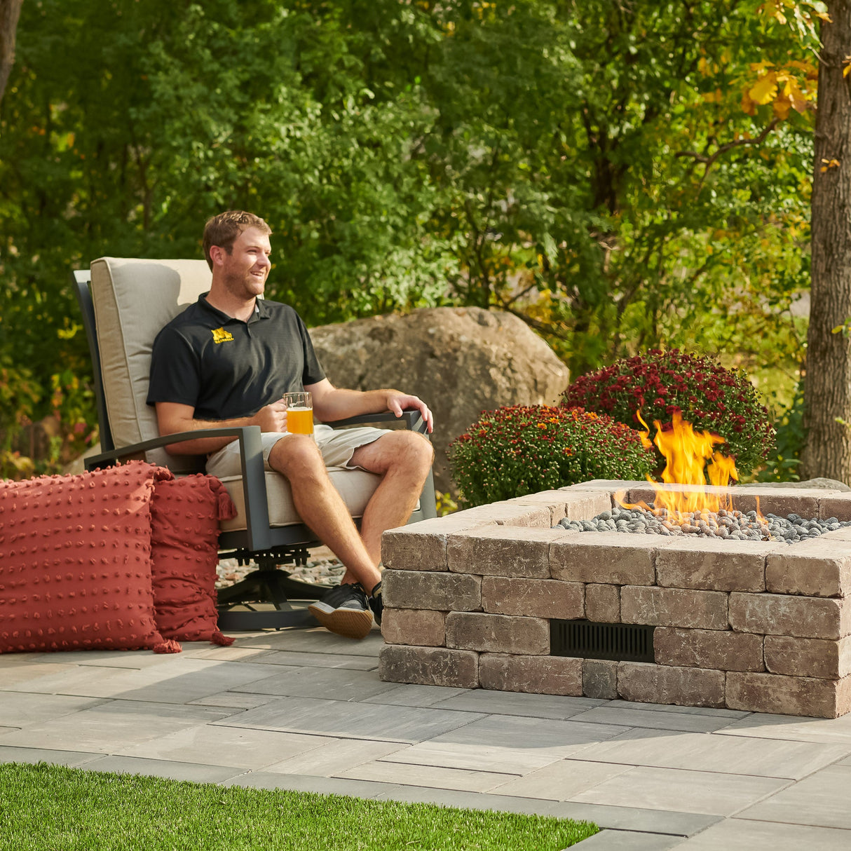 An individual sitting next to the Bronson Block Square Gas Fire Pit Kit