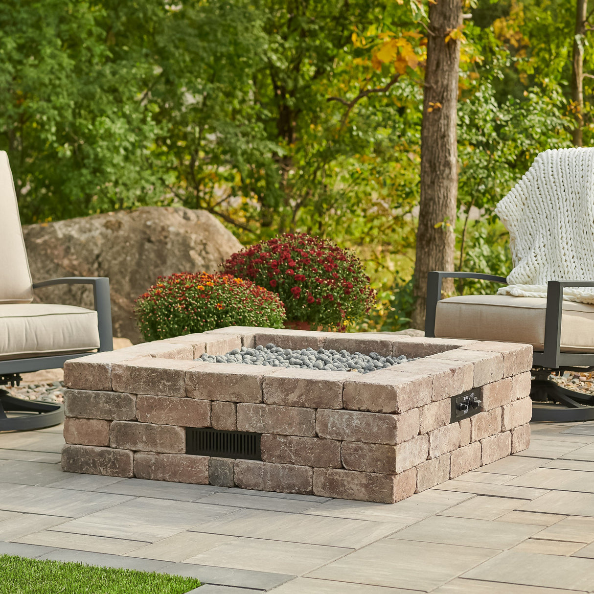 The Bronson Block Square Gas Fire Pit Kit with lava rocks on the burner sitting in an outdoor space