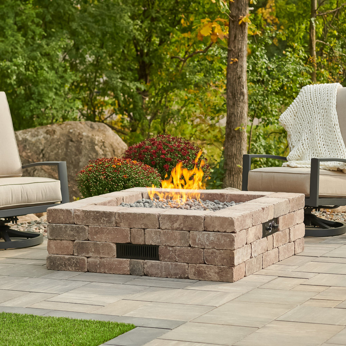 The Bronson Block Square Gas Fire Pit Kit in a scenic patio setting surrounded by patio furniture