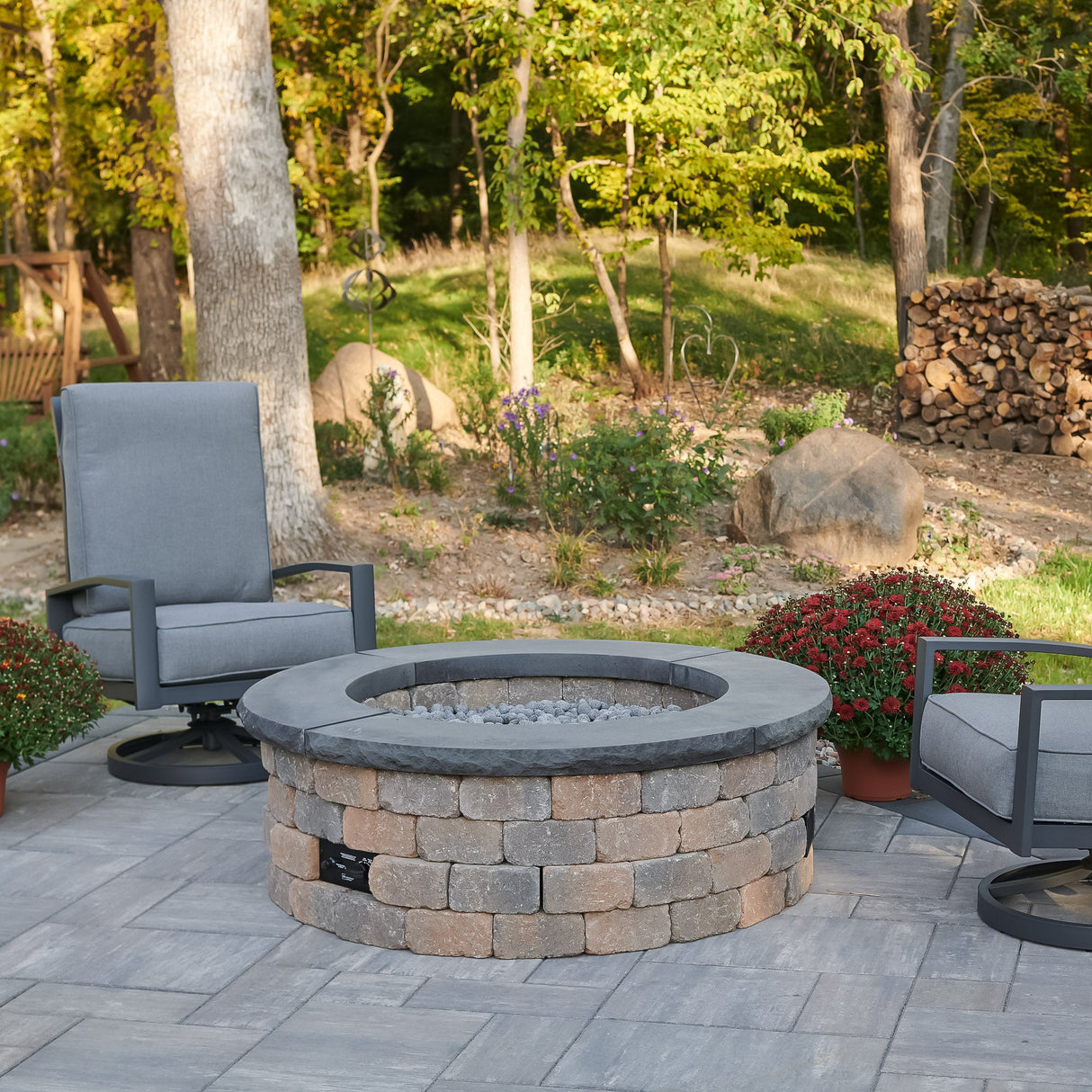 The Bronson Block Round Gas Fire Pit Kit sitting in an outdoor space surrounded by lounge chairs
