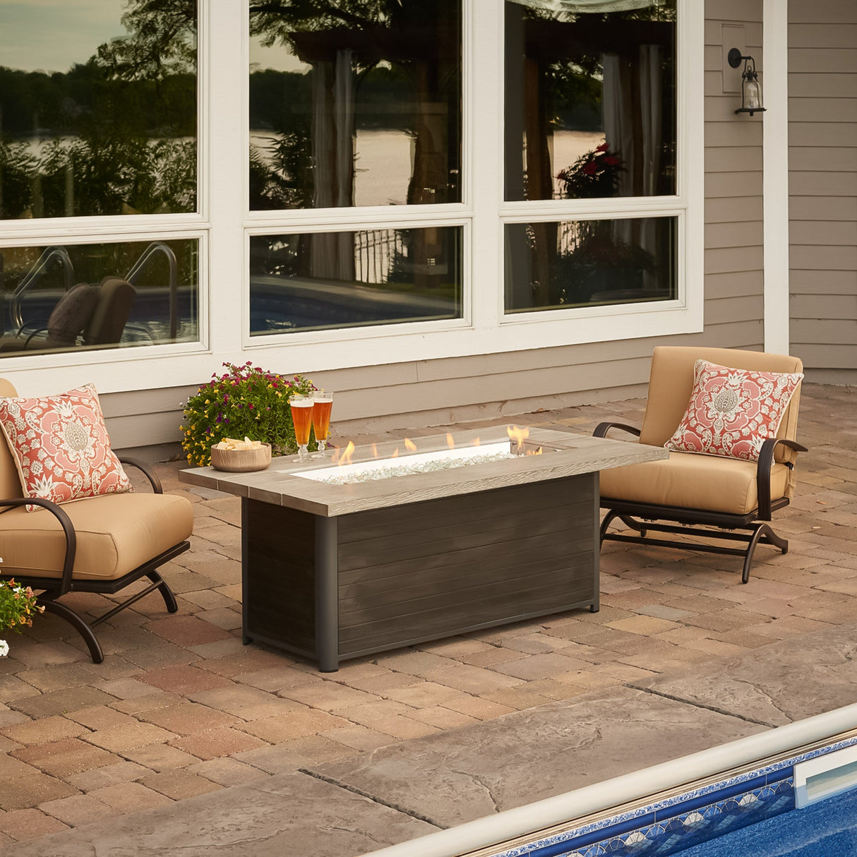 The Cedar Ridge Linear Gas Fire Pit Table in a patio setting, next to furniture and a pool