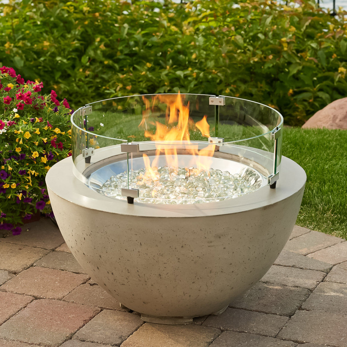A glass wind guard on a Cove Round Gas Fire Pit Bowl 29" while in an outdoor space