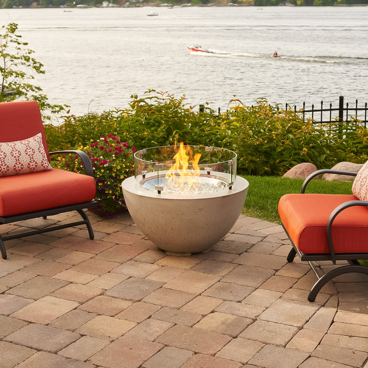 A Cove Round Gas Fire Pit Bowl 29" next to a lake on a scenic patio setup with outdoor furniture