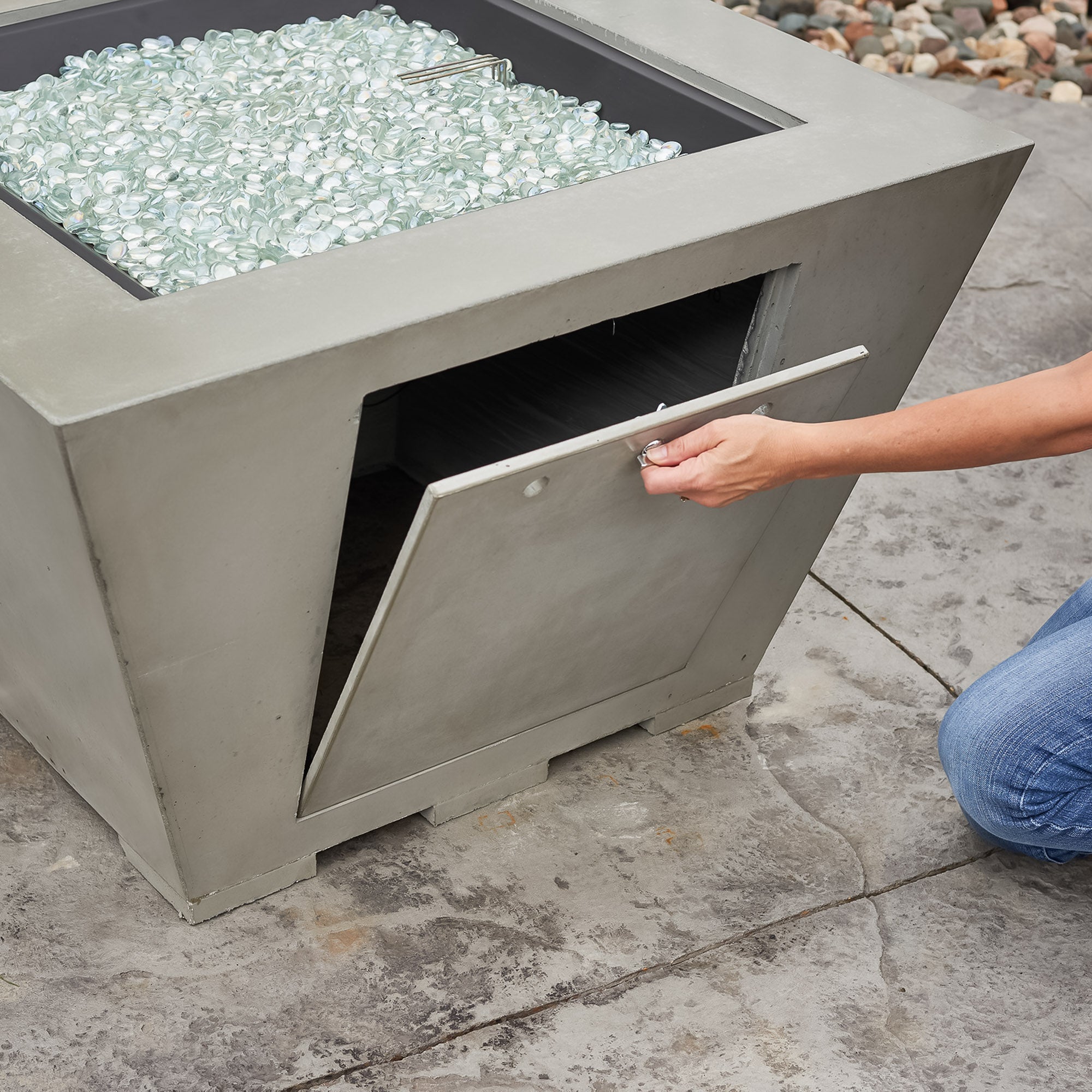 An individual opening the side access door of the Cove Square Gas Fire Pit Bowl