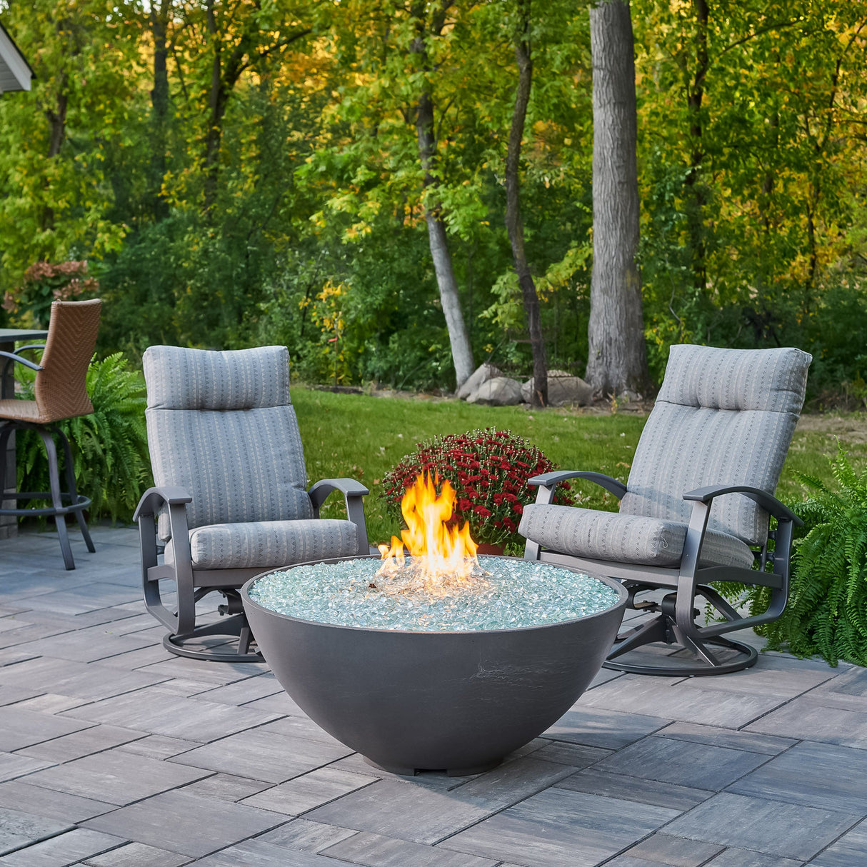 A Midnight Mist Cove Edge Round Gas Fire Pit Bowl 42" with a large flame and surrounded by patio furniture