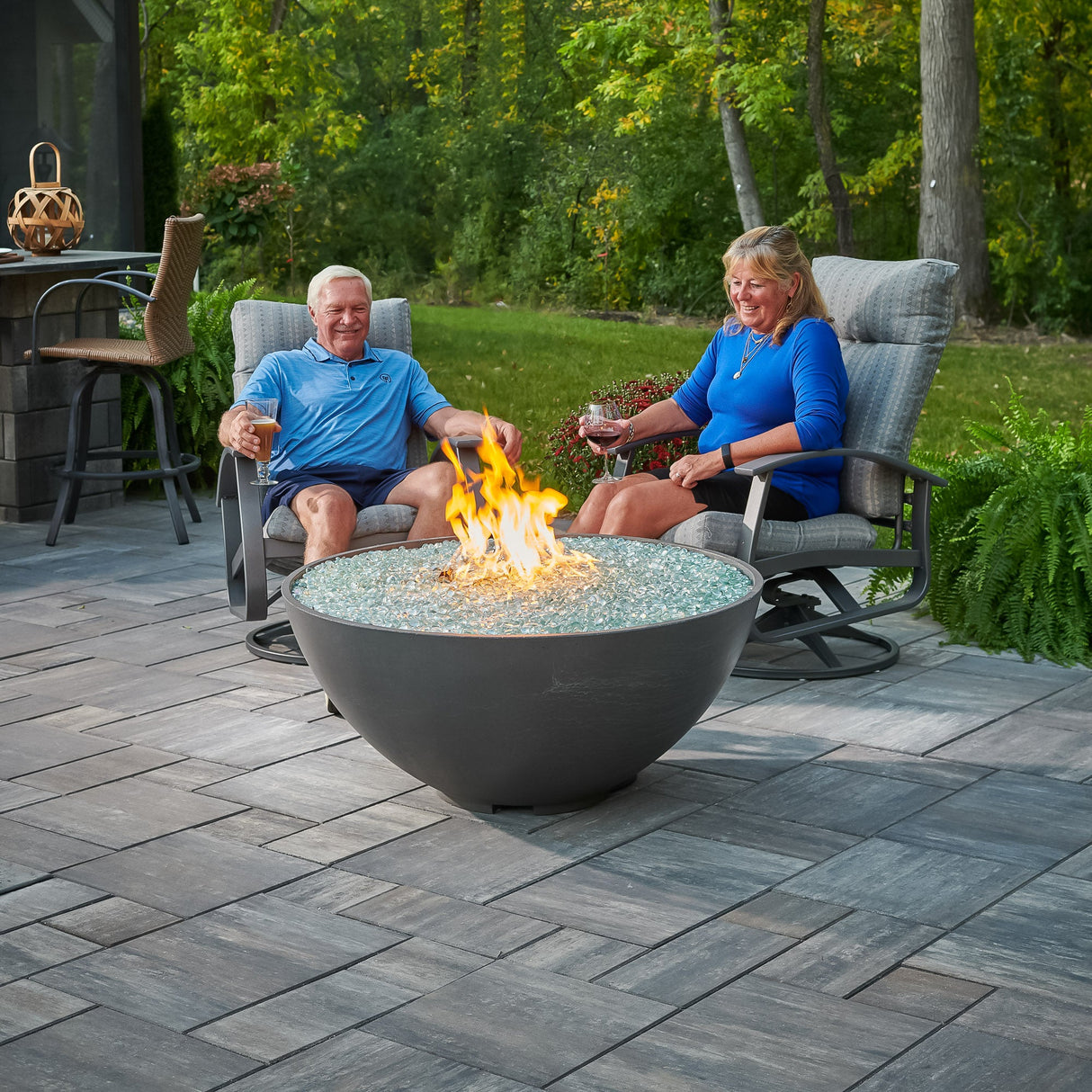 Two individuals relaxing next to a Midnight Mist Cove Edge Round Gas Fire Pit Bowl 42" in their backyard