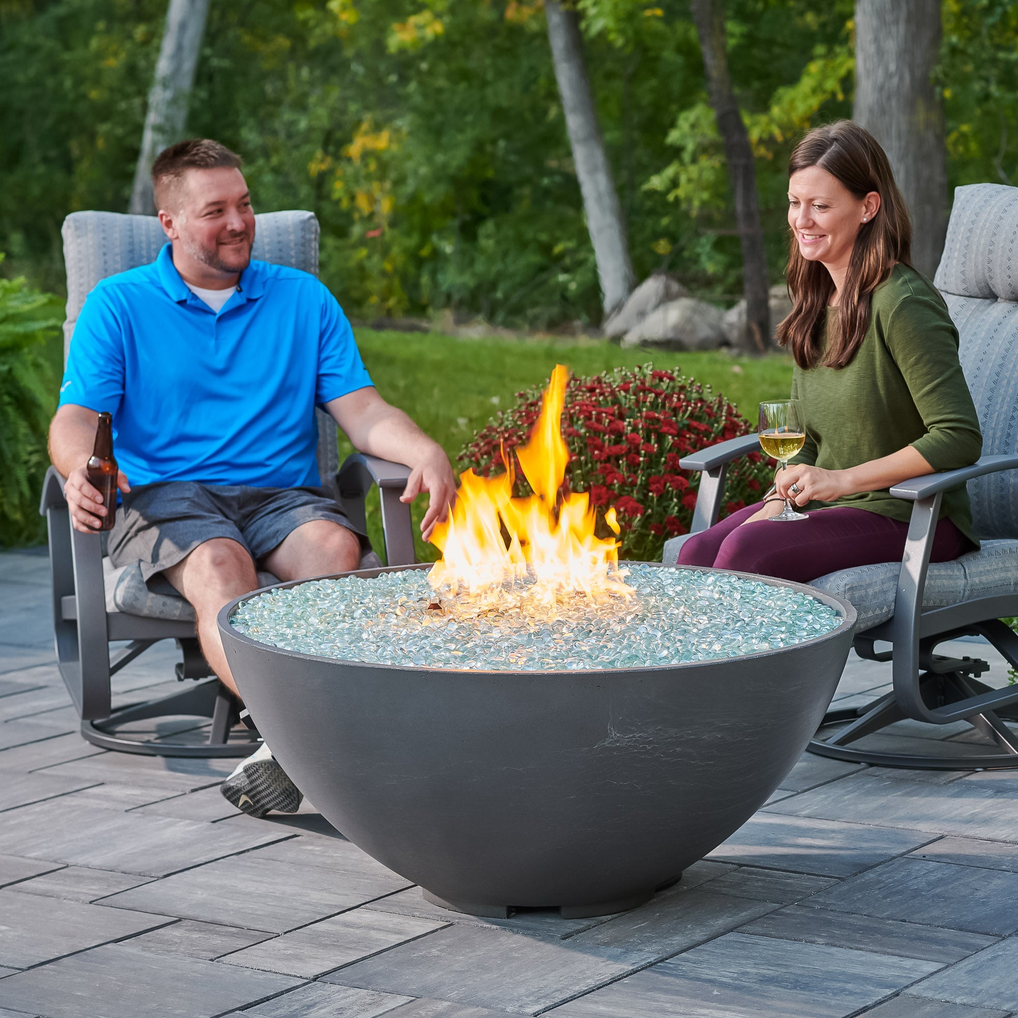 Two individuals relaxing next to a Midnight Mist Cove Edge Round Gas Fire Pit Bowl 42" on a patio