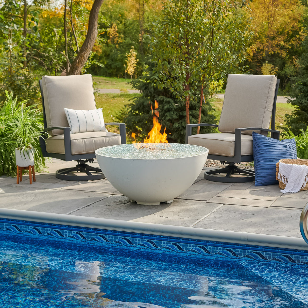 A White Cove Edge Round Gas Fire Pit Bowl 42" next to a pool and lounge chairs