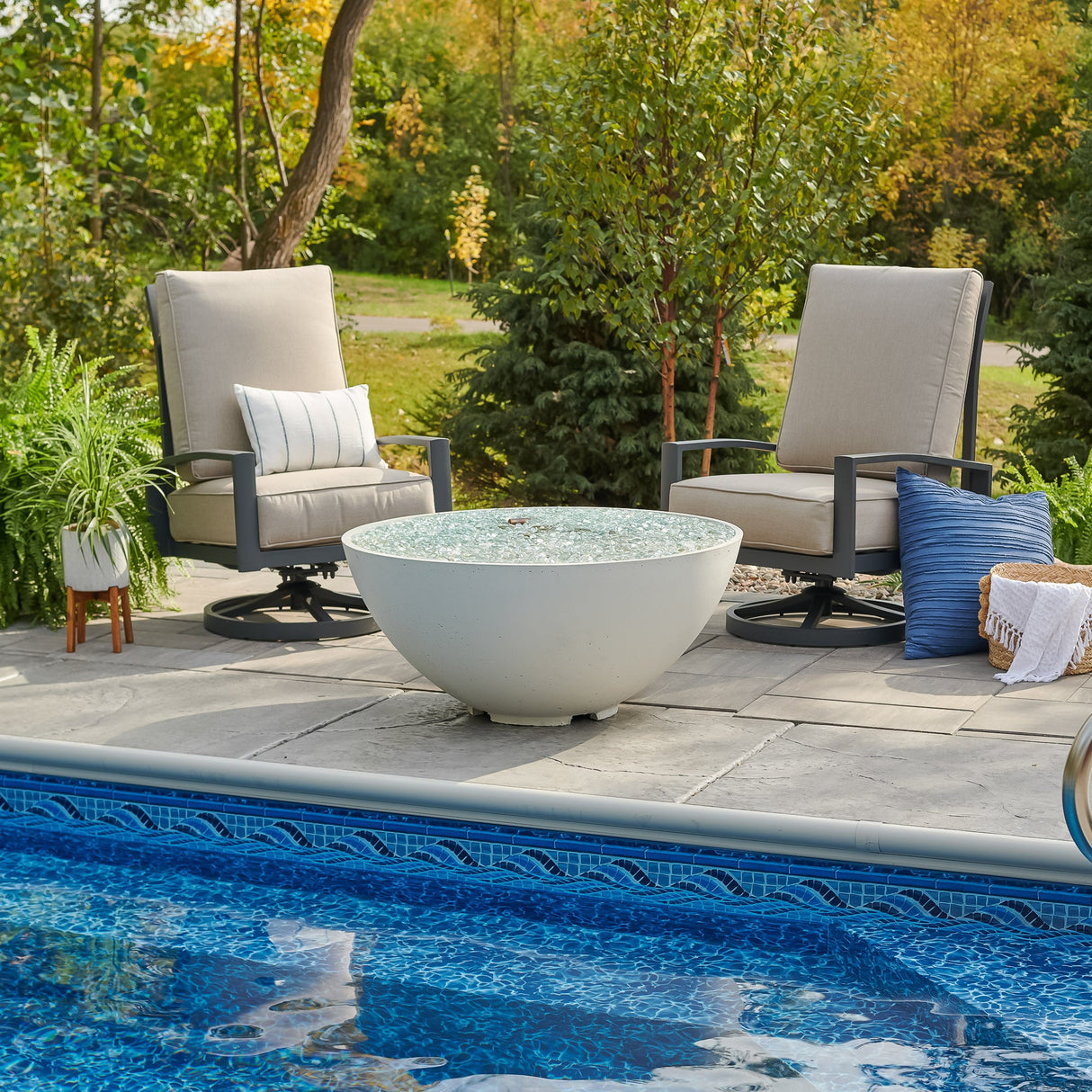 A White Cove Edge Round Gas Fire Pit Bowl 42" next to a pool in a scenic backyard