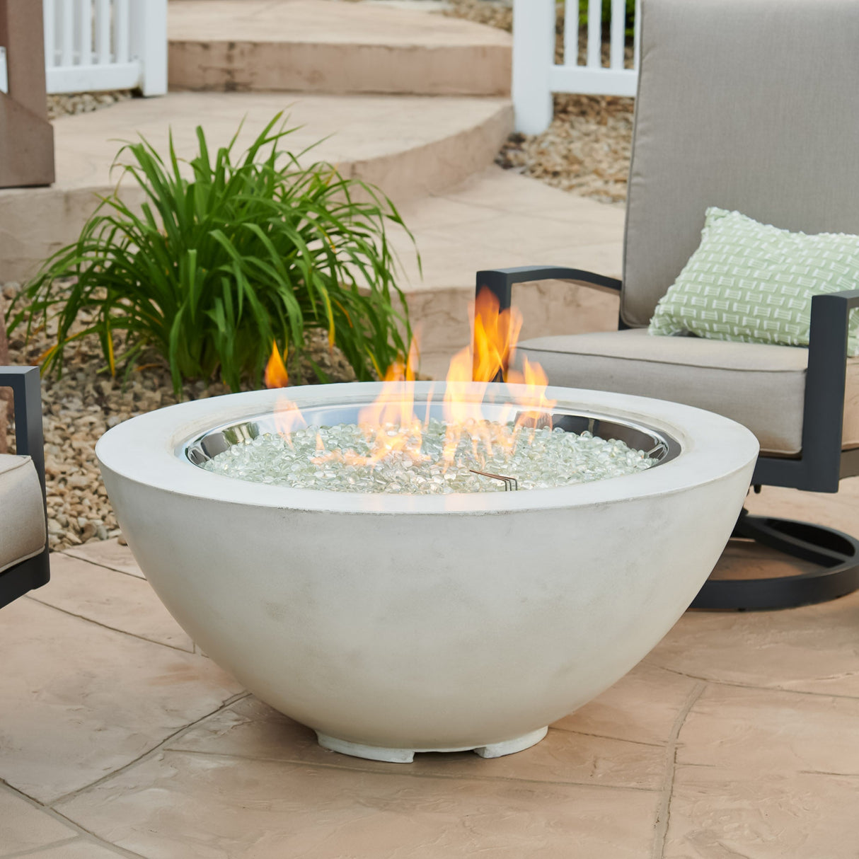 A White Cove Round Gas Fire Pit Bowl 42" placed around patio furniture