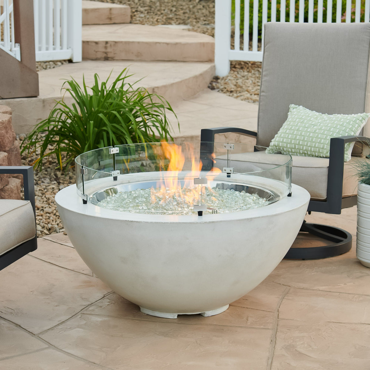 A glass wind guard on a White Cove Round Gas Fire Pit Bowl 42" while it is operating outside