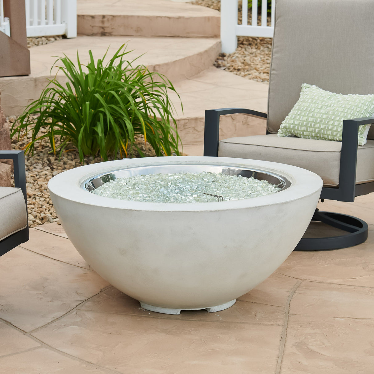 A White Cove Round Gas Fire Pit Bowl 42" with fire media on the burner and surrounded by patio furniture