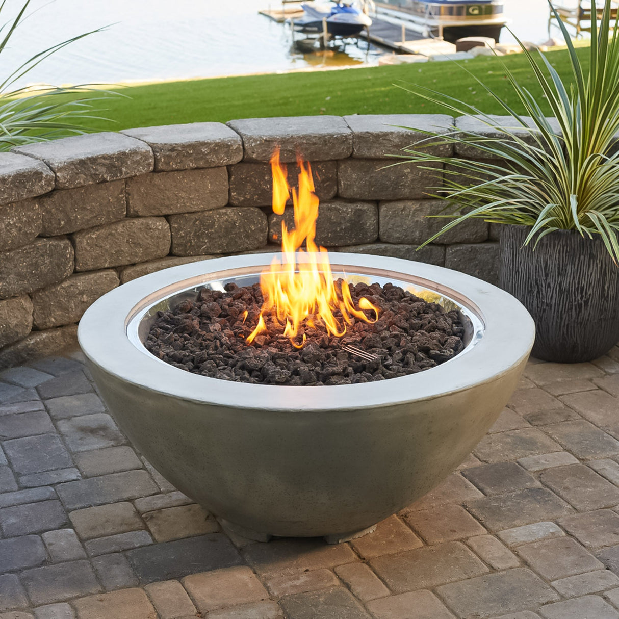 A Natural Grey Cove Round Gas Fire Pit Bowl 42" next a lake on a patio setting