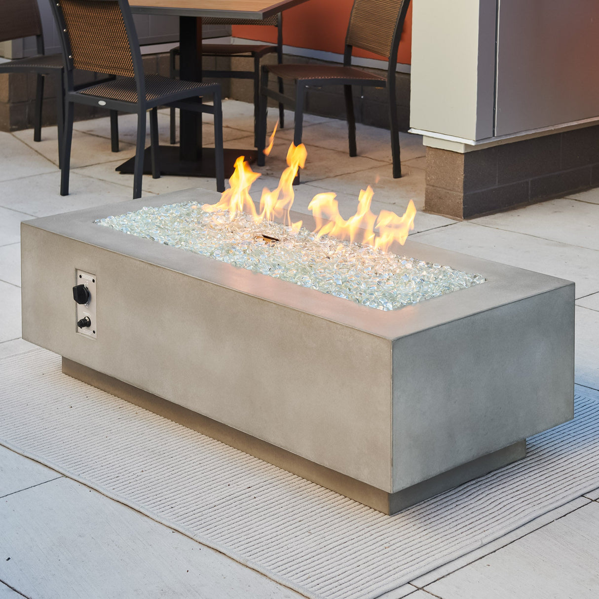 A Natural Grey Cove Linear Gas Fire Pit Table 54" with a large flame coming from the burner