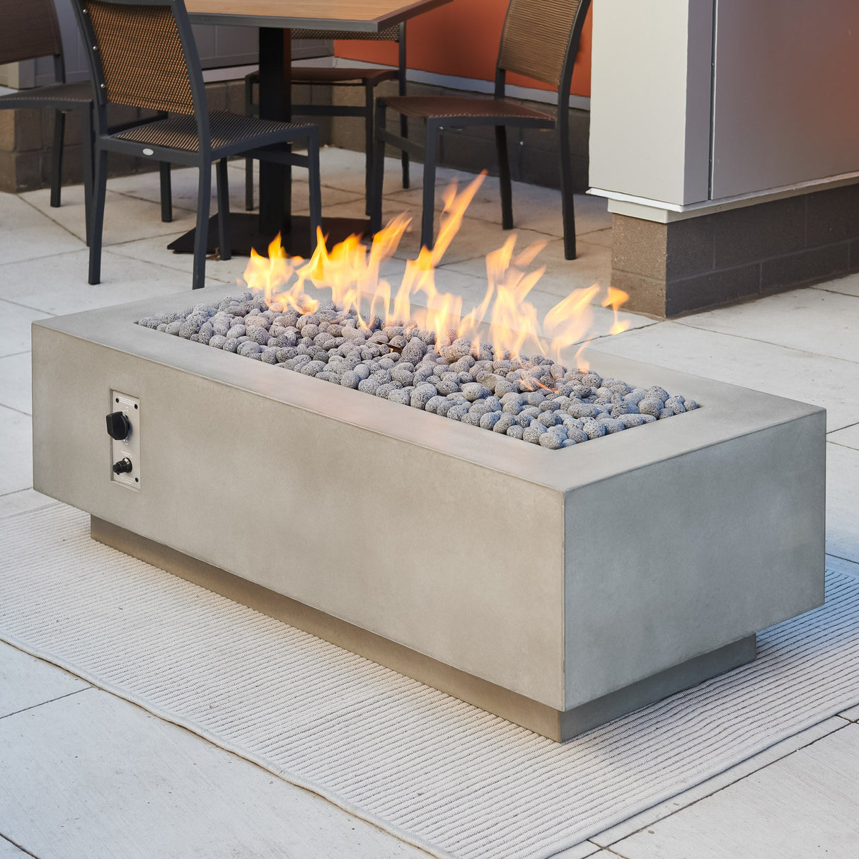 Lava rocks and a large flame on the Natural Grey Cove Linear Gas Fire Pit Table 54"