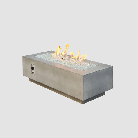 A Natural Grey Cove Linear Gas Fire Pit Table 54" with a large flame coming from the burner surrounded by a white background