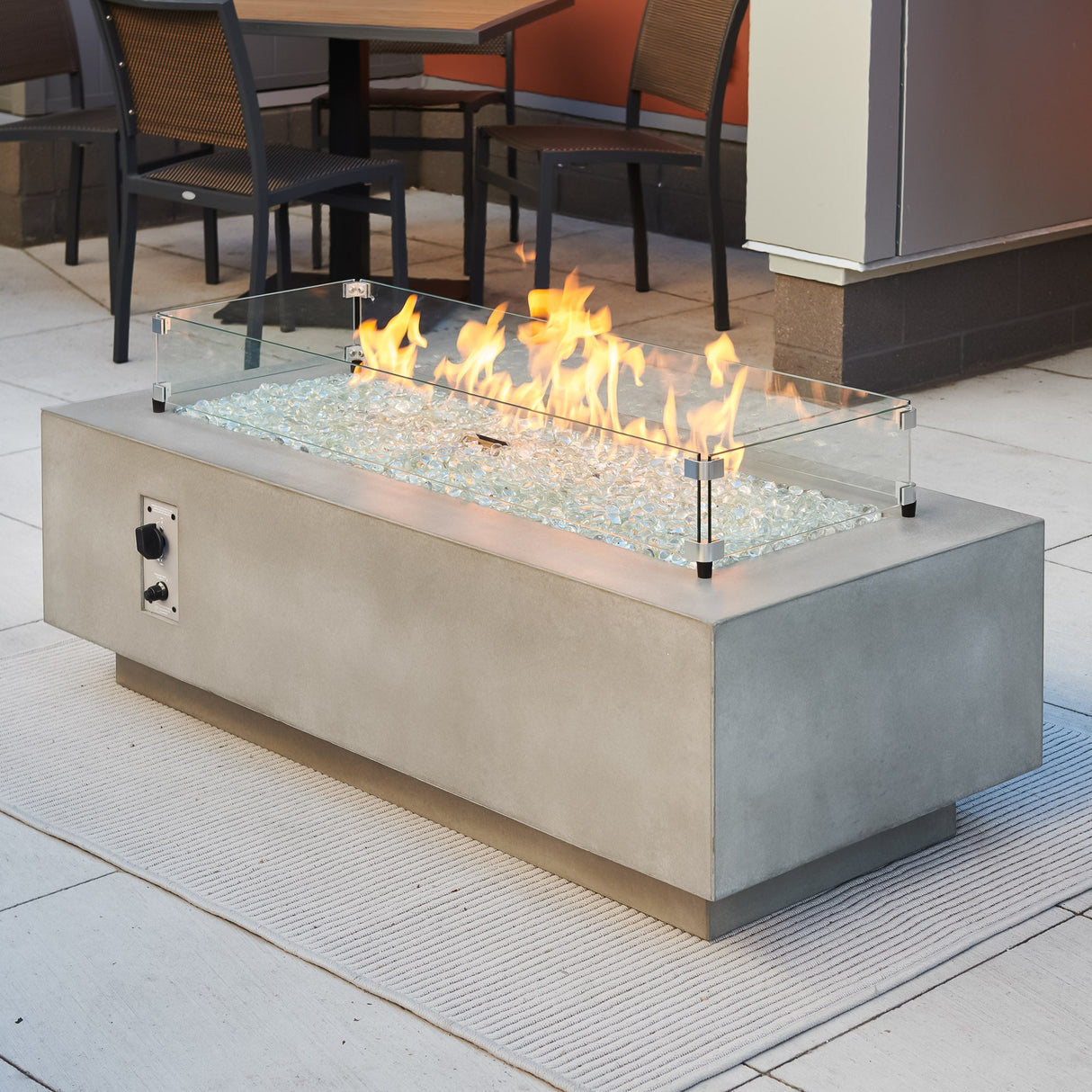 A glass wind guard placed on the top of a Natural Grey Cove Linear Gas Fire Pit Table 54"