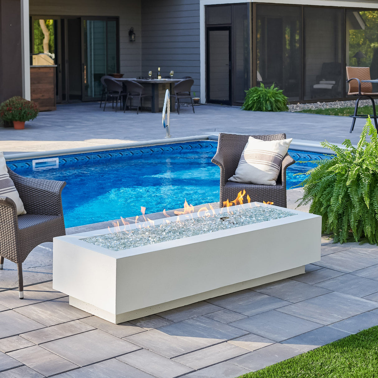 A scenic patio with the White Cove Linear Gas Fire Pit Table 72", patio furniture, and plants