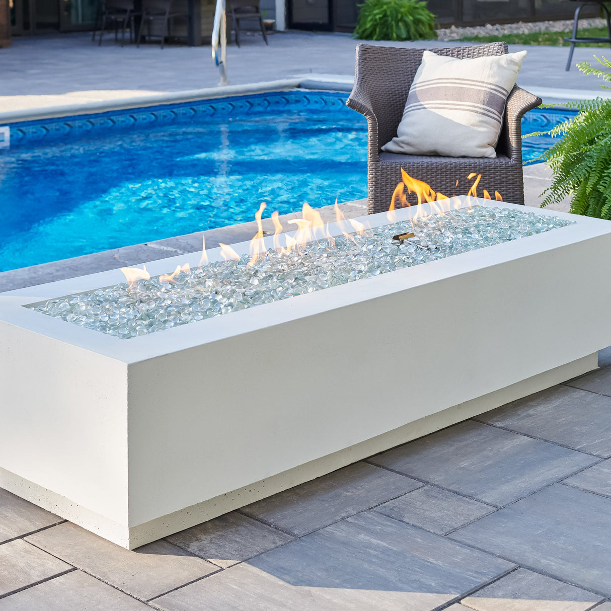 A White Cove Linear Gas Fire Pit Table 72" next to a large pool and patio furniture